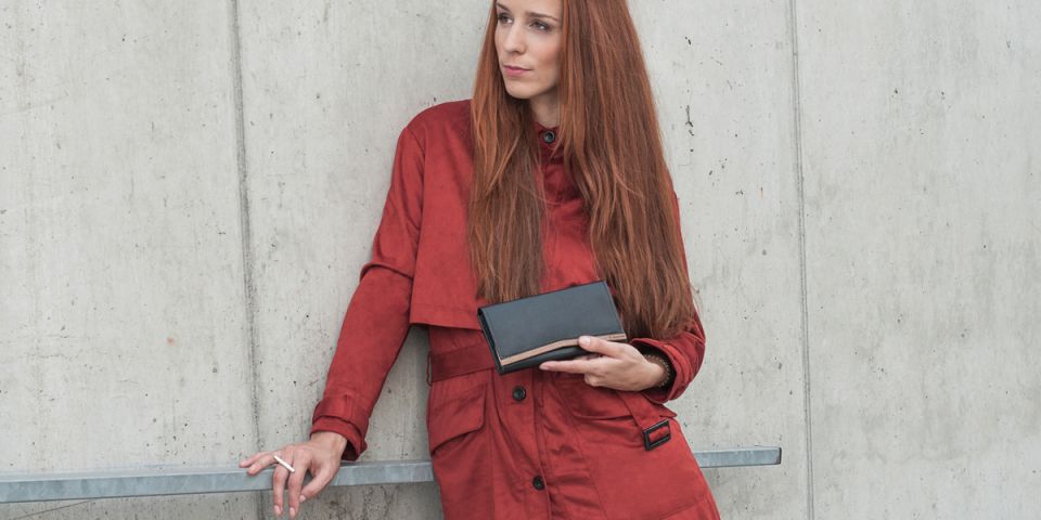 Ruda kobieta w pomarańczowym płaszczu, trzymająca skórzany portfel Caleo Woman Wallet Ruda kobieta w pomarańczowym płaszczu, trzymająca skórzany portfel Caleo Woman Wallet