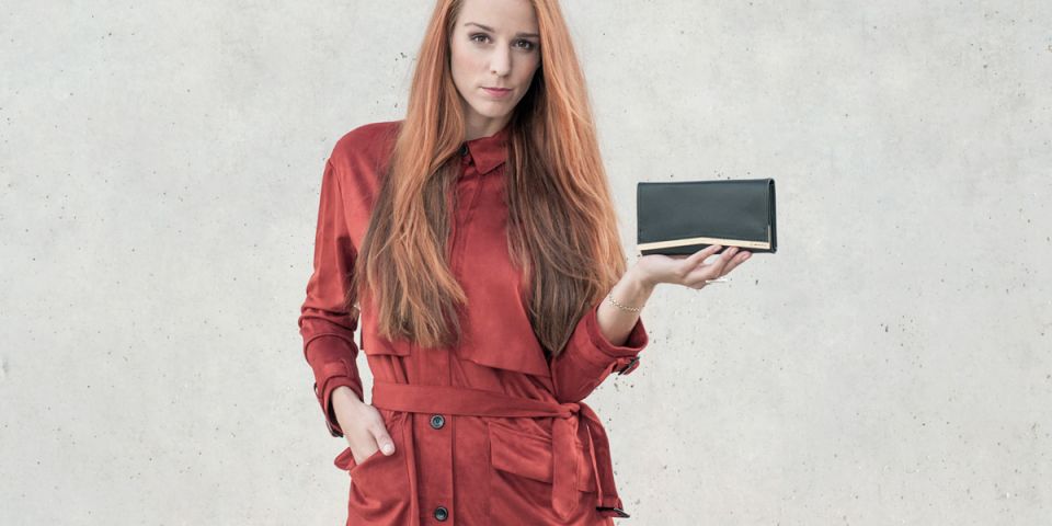 Ruda kobieta w pomarańczowym płaszczu, trzymająca skórzany portfel Liti Woman Wallet Ruda kobieta w pomarańczowym płaszczu, trzymająca skórzany portfel Liti Woman Wallet